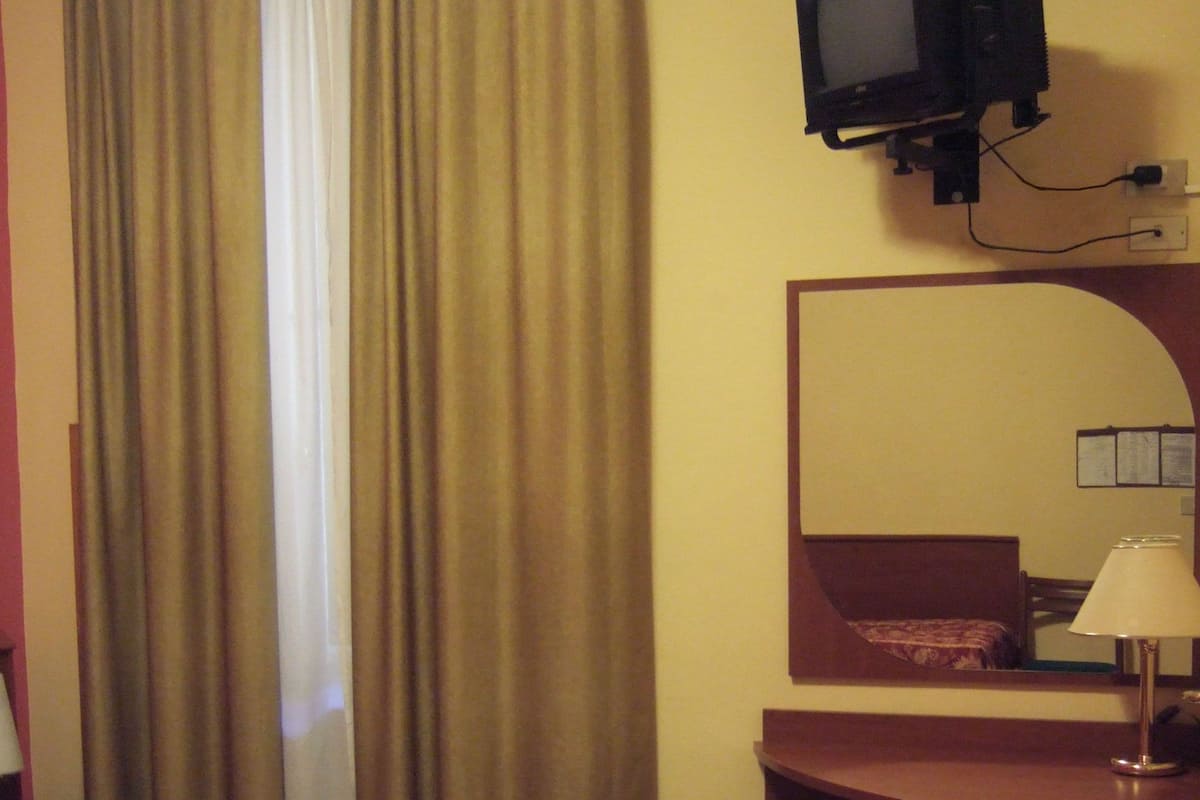 Habitació d'hotel amb un llit, una taula de treball, una televisió, una làmpada i un mirall.