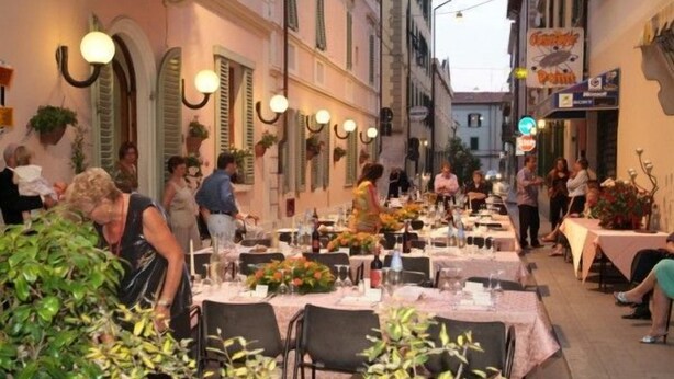 An outdoor dining area with tables set for guests, surrounded by buildings with traditional architecture and hanging lights. - Innocenti (Montecatini Terme)