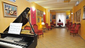 A grand piano with sheet music, red upholstered chairs, and a dining area with a table and chairs. - Innocenti (Montecatini Terme)