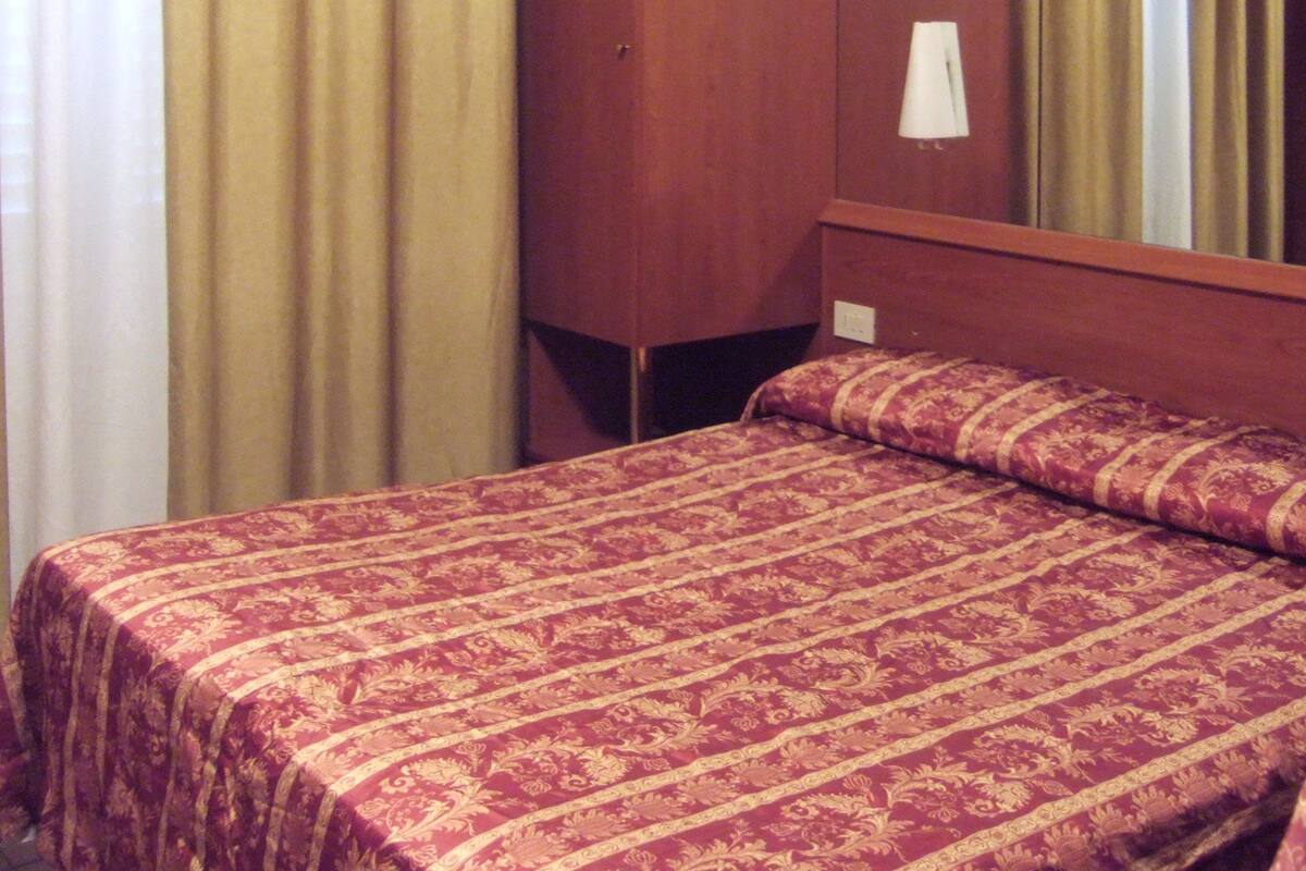 Habitació d'hotel amb un llit individual, un armari de fusta i un mirall gran.