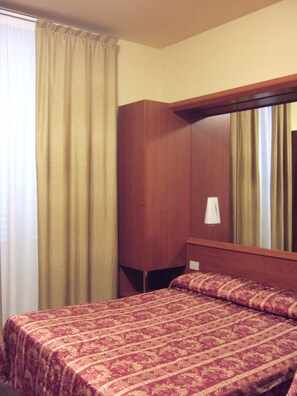 A hotel room with a single bed, a wooden wardrobe, and a large mirror. - Innocenti (Montecatini Terme)