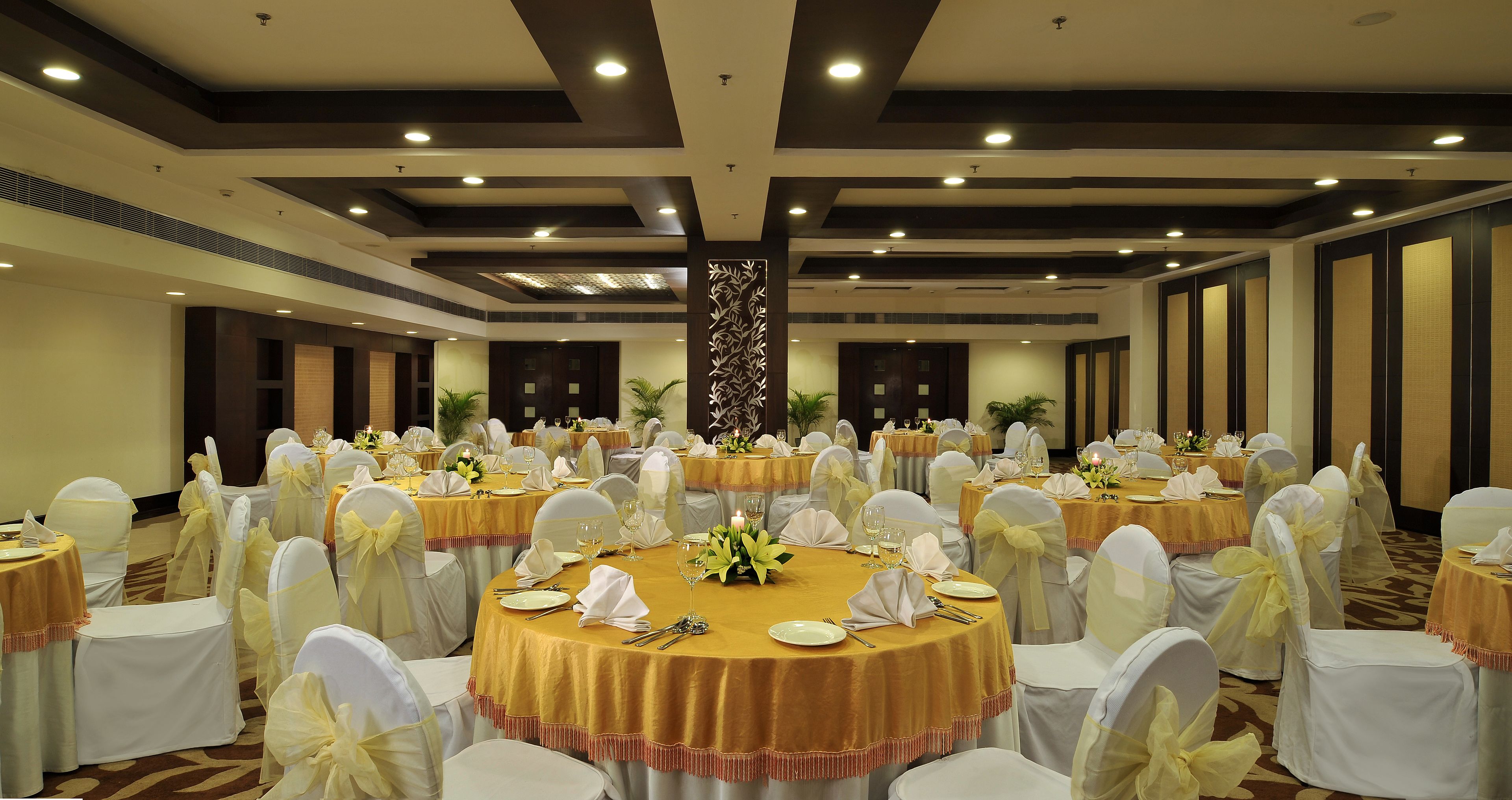 A banquet hall with round tables, white chairs, and yellow tablecloths.