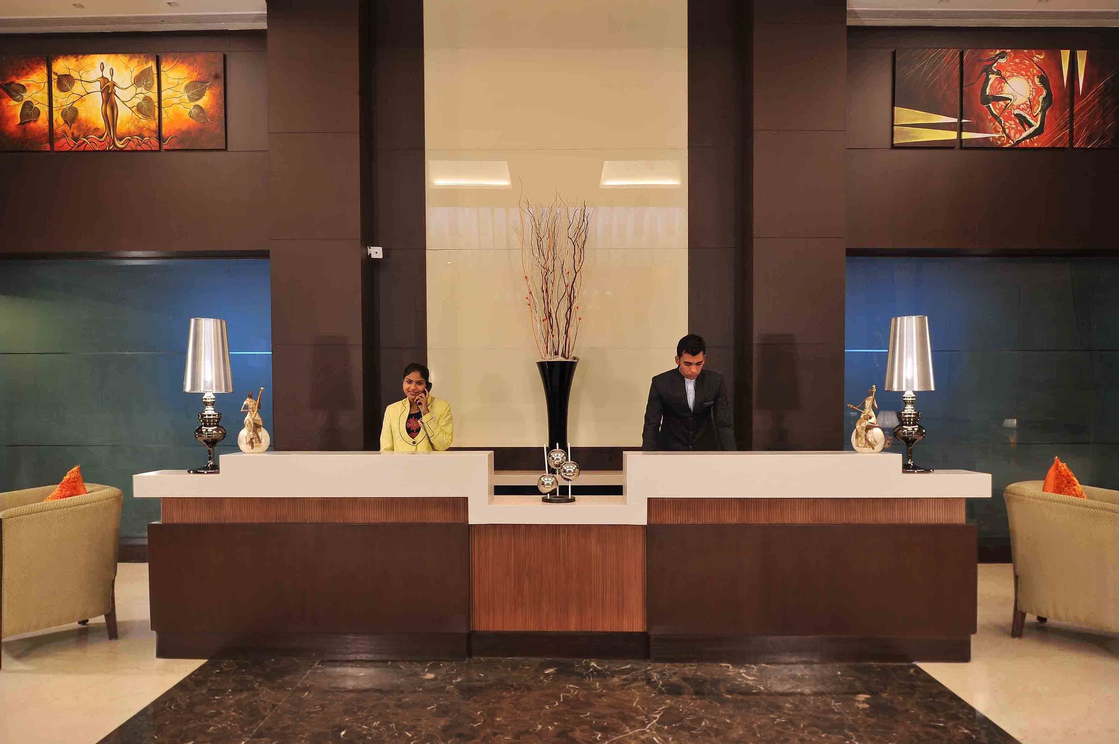 A reception area with two receptionists, a central decorative vase, and two side tables with lamps.