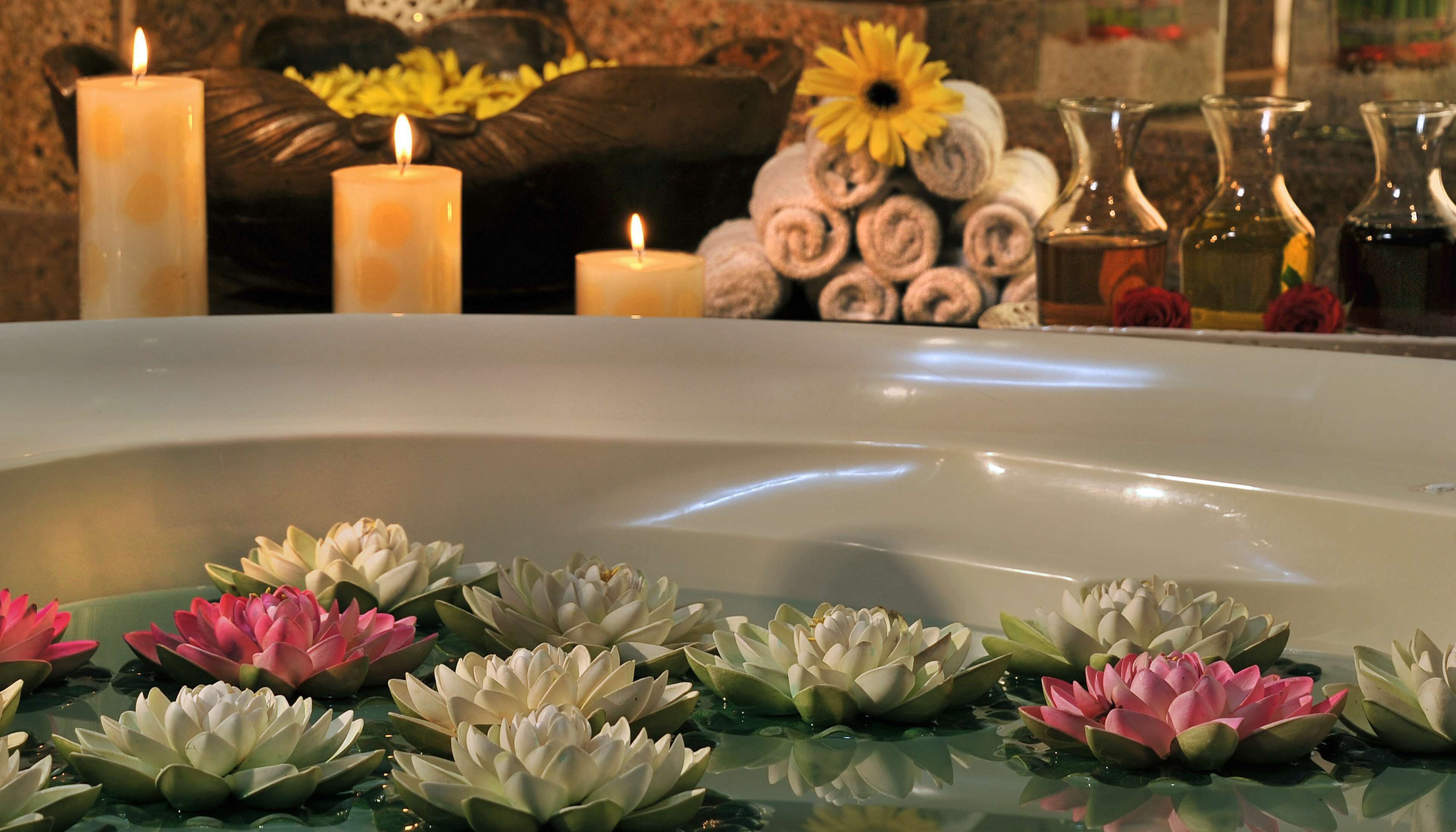 A spa setting with a bathtub, candles, and lotus flowers.