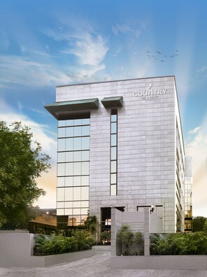 A modern building with a sign reading 'Country Inn & Suites by Radisson.' It features a prominent entrance with a glass facade and a landscaped area with greenery.