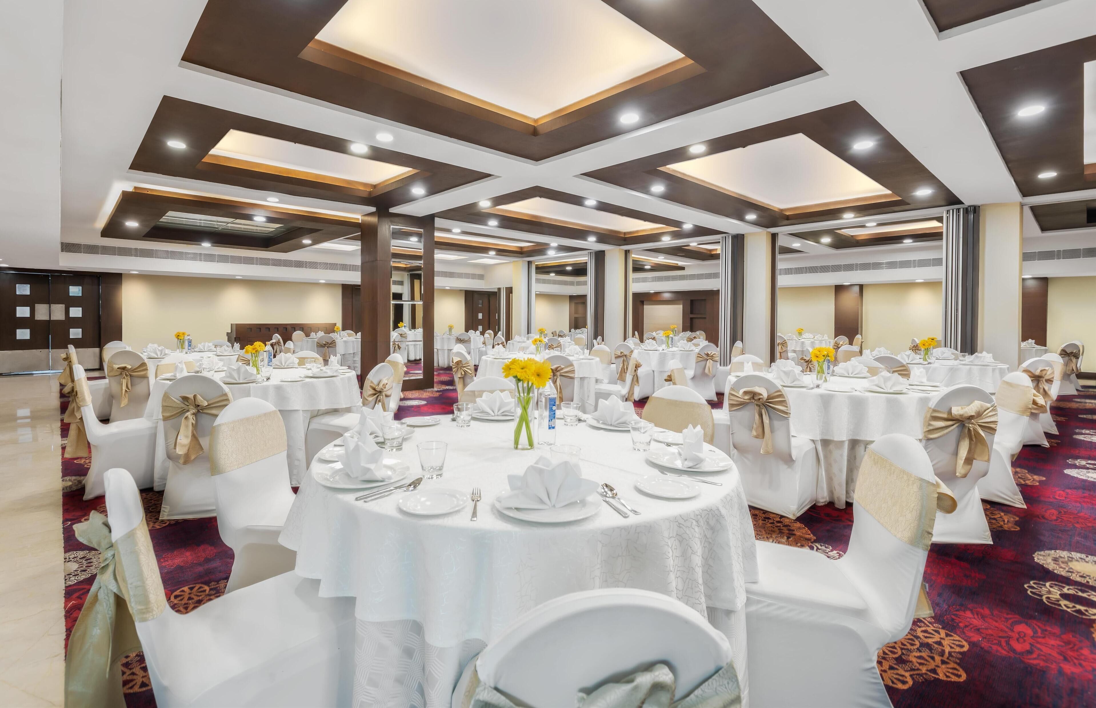 A banquet hall with round tables, white chairs, and yellow flowers.