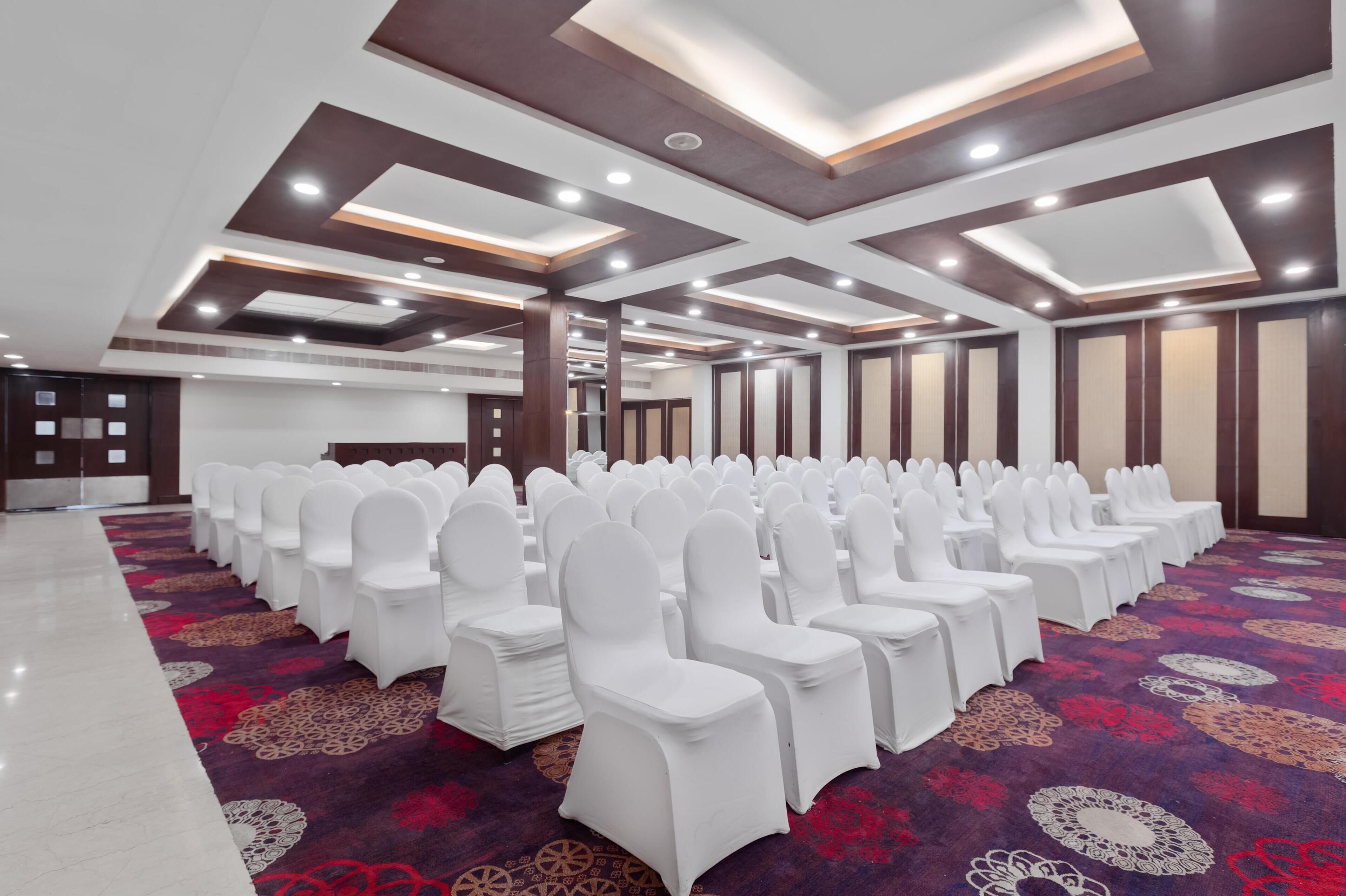 A conference room with rows of white chairs and a patterned carpet.