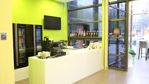 Een receptiegedeelte met een wit aanrecht, een aan de muur bevestigde televisie en een raam met planken waarop flessen staan.
