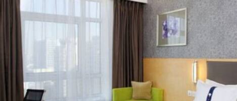 A hotel room with a bed, a green sofa, a chair, a small table, and a window with curtains.