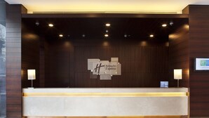 Een modern receptiebalie met een Holiday Inn Express bord, een flatscreen televisie en twee wandlampen.