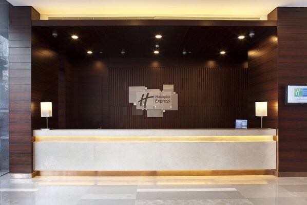 A modern reception desk with a Holiday Inn Express sign, a flat-screen TV, and two wall-mounted lamps.