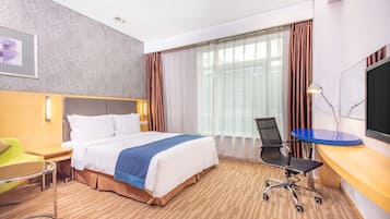 Habitación de hotel con cama, escritorio, silla, televisión y ventana con cortinas.