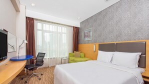 Een hotelkamer met een groot bed, een bureau met een computer, een stoel en een klein tafeltje.