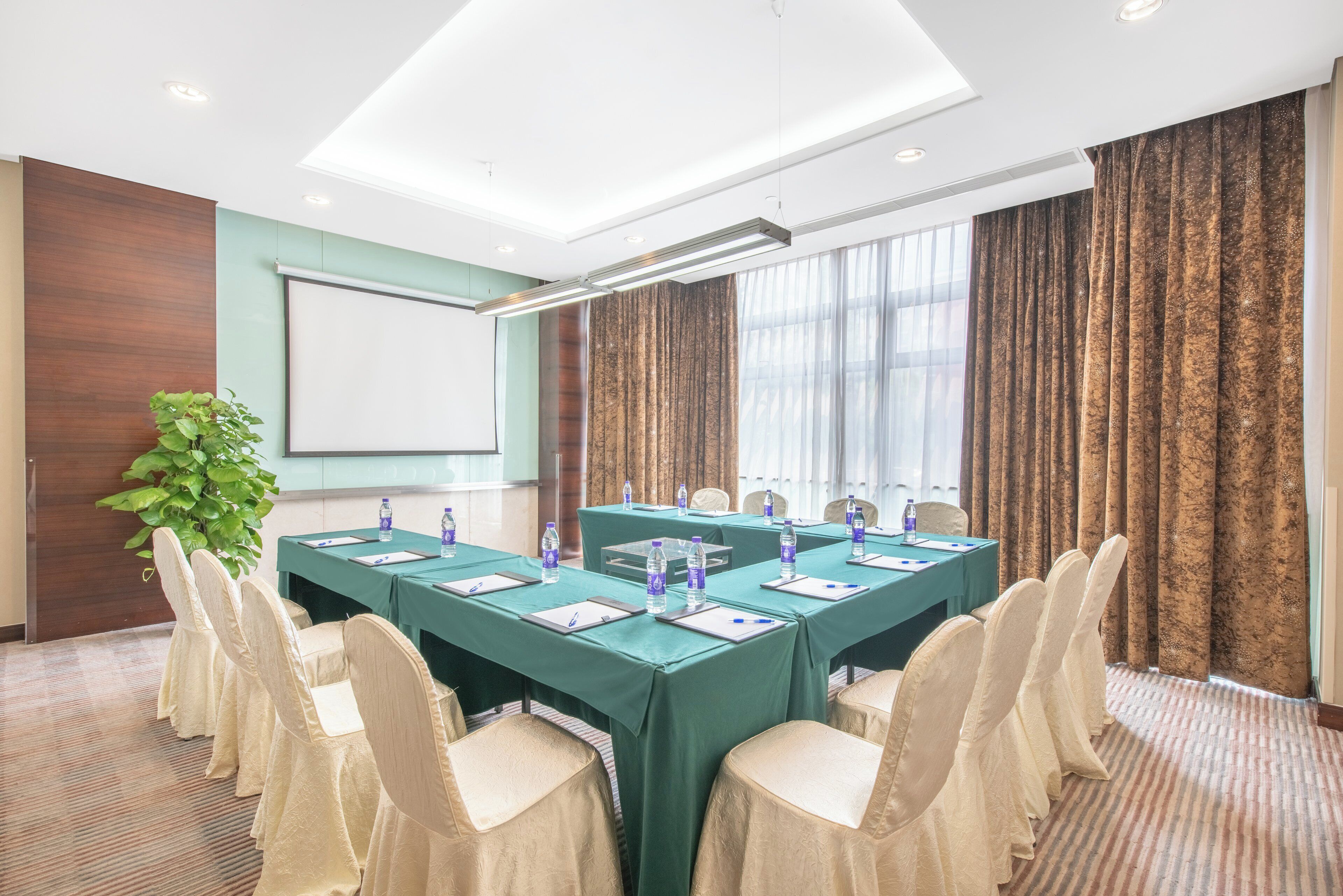 A conference room with a long table, chairs, a projector screen, and a large window with curtains.