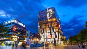 Un edificio moderno con grandes ventanales y señalización iluminada de Adidas y UNIQLO.