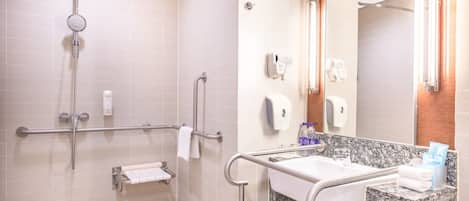 Un baño moderno con ducha, barras de apoyo, lavamanos con encimera de mármol y espejo.