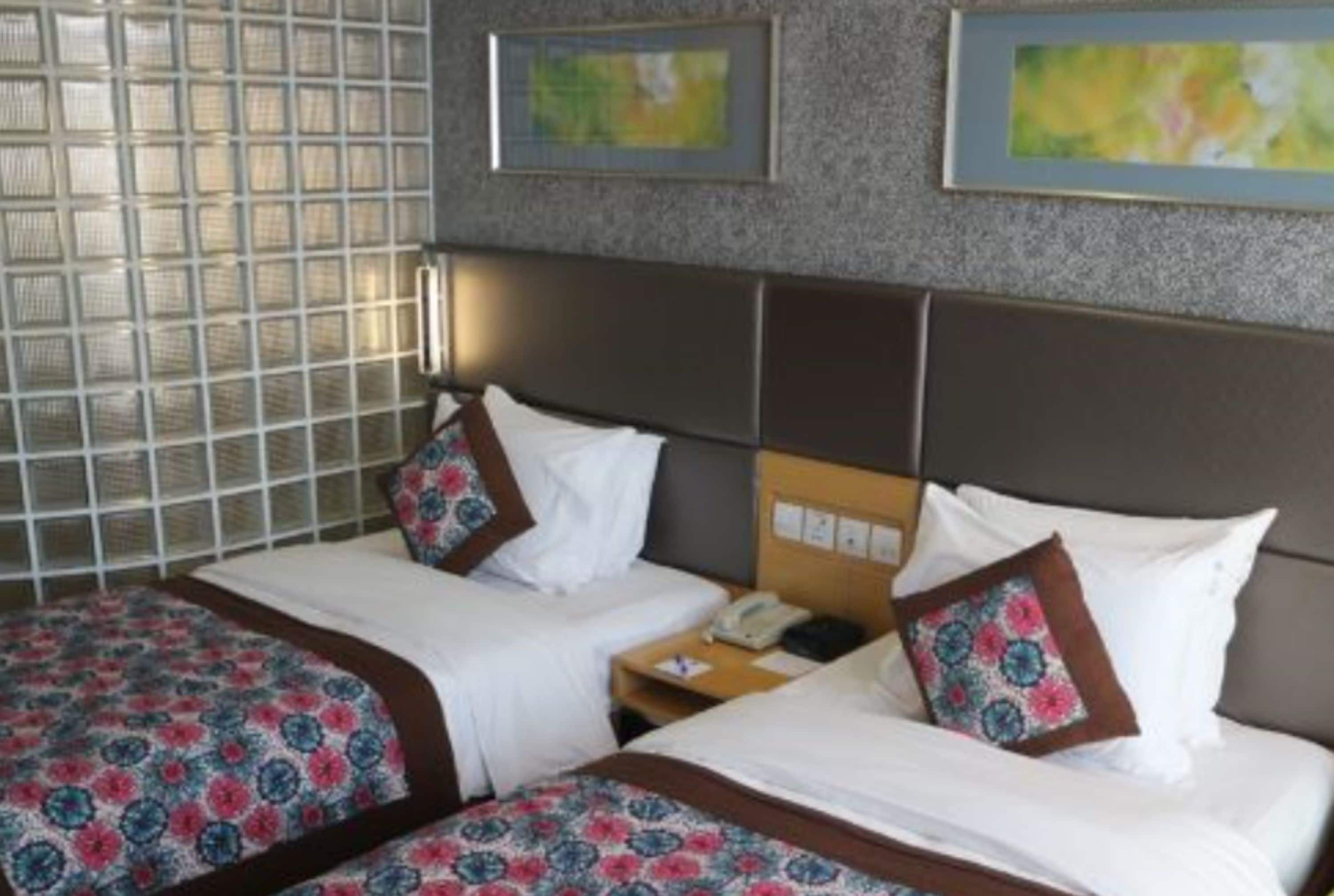 A hotel room with two beds, a nightstand, and a wall-mounted telephone.