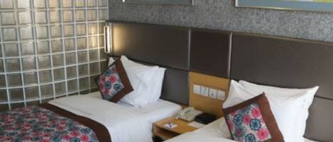 A hotel room with two beds, a nightstand, and a wall-mounted telephone.