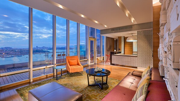 Een moderne hotelkamer met een ruim balkon, een zithoek met een bank en stoelen, en uitzicht op de stad en het water.