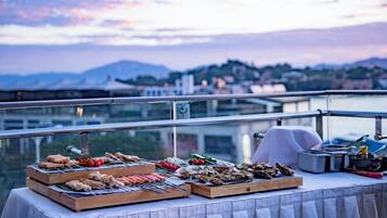 A buffet table with various food items on a balcony overlooking a cityscape.