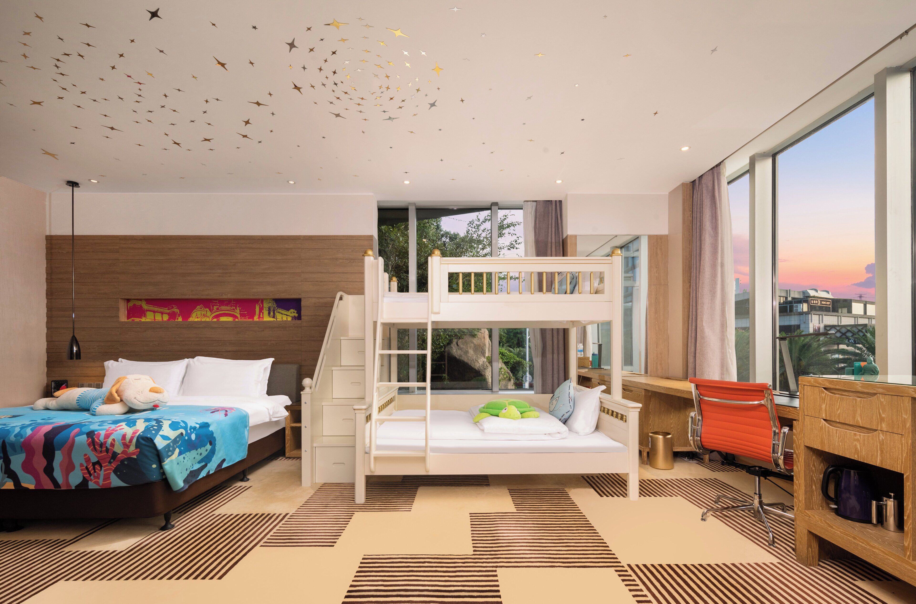 Ein modernes Hotelzimmer mit Etagenbett, Schreibtisch und großem Fenster mit Blick auf die Stadt.