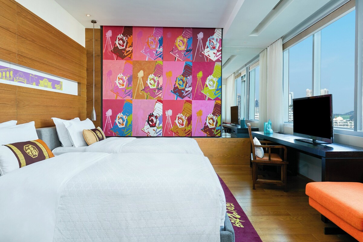 Een hotelkamer met een groot bed, een bureau met een computer, een televisie en uitzicht over de stad.