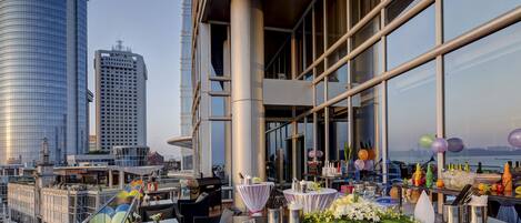 Un bar situé sur un toit, avec des tables aménagées pour les repas, offrant une vue panoramique sur la ville et ses grands immeubles.