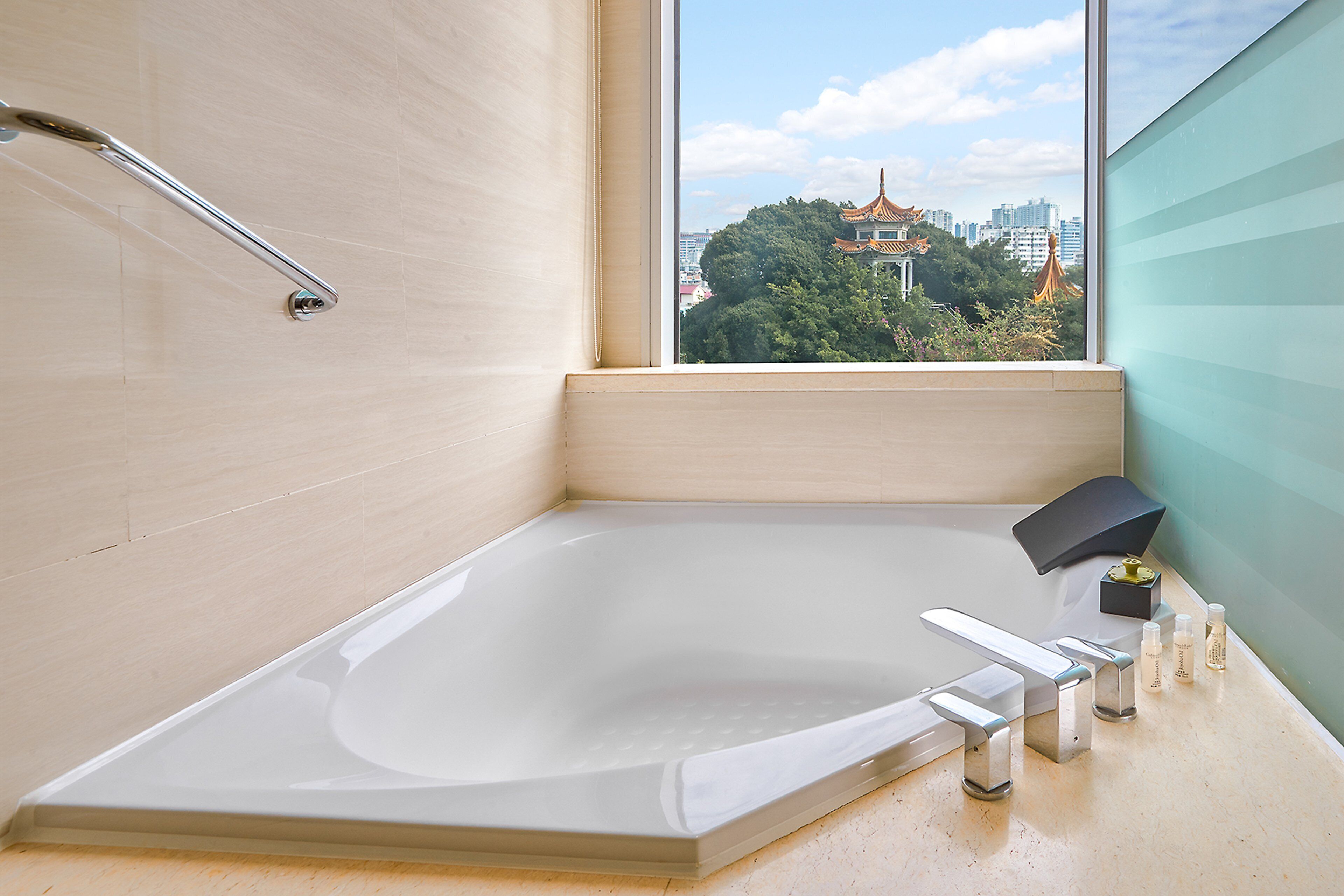 A modern bathroom with a large bathtub, a window with a city view, and a towel rack.