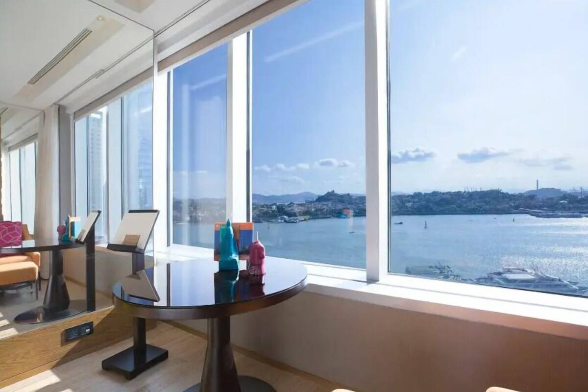 Una habitación moderna con ventanas amplias que ofrecen vista a un cuerpo de agua y colinas distantes.