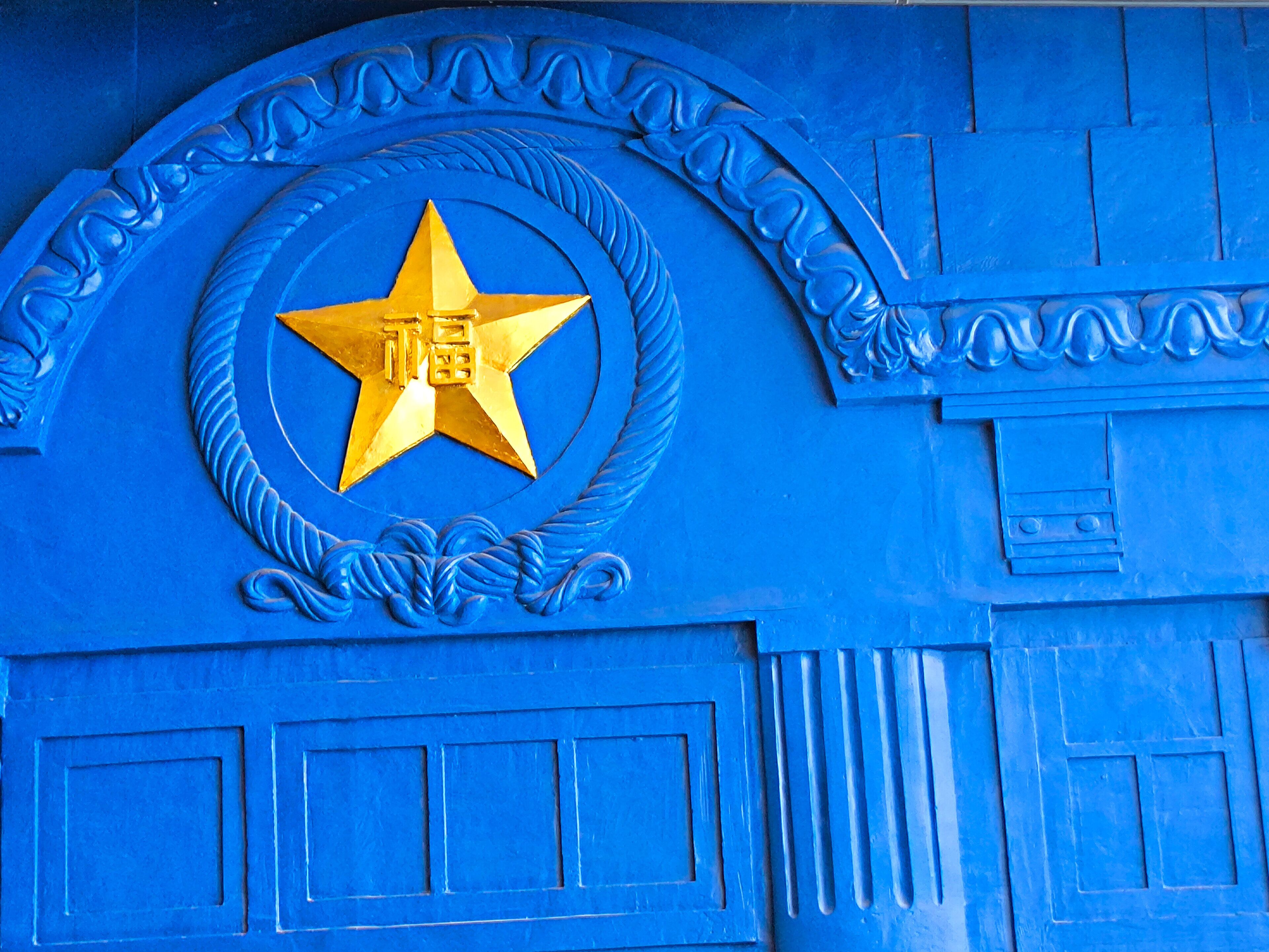 Uma porta azul com emblema dourado em formato de estrela e molduras decorativas.