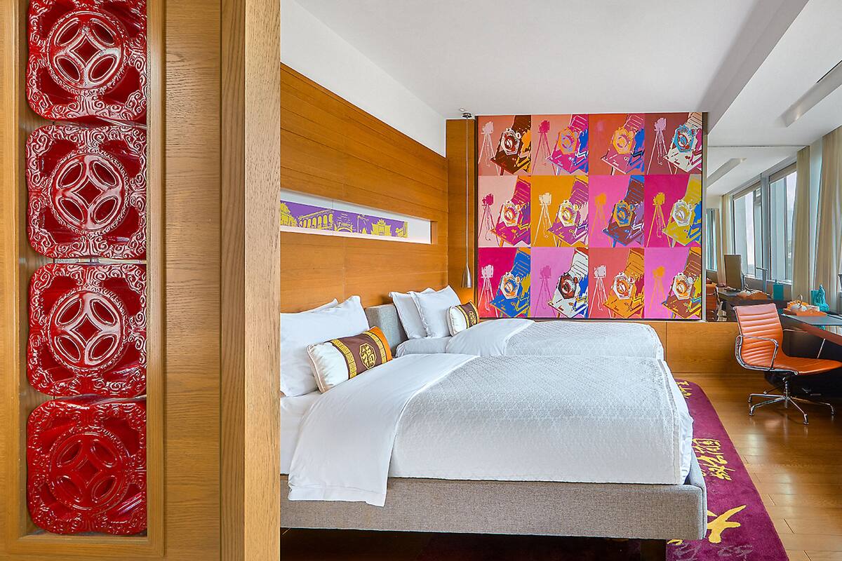Una habitación de hotel moderna con una cama grande, un escritorio con una computadora y un televisor.