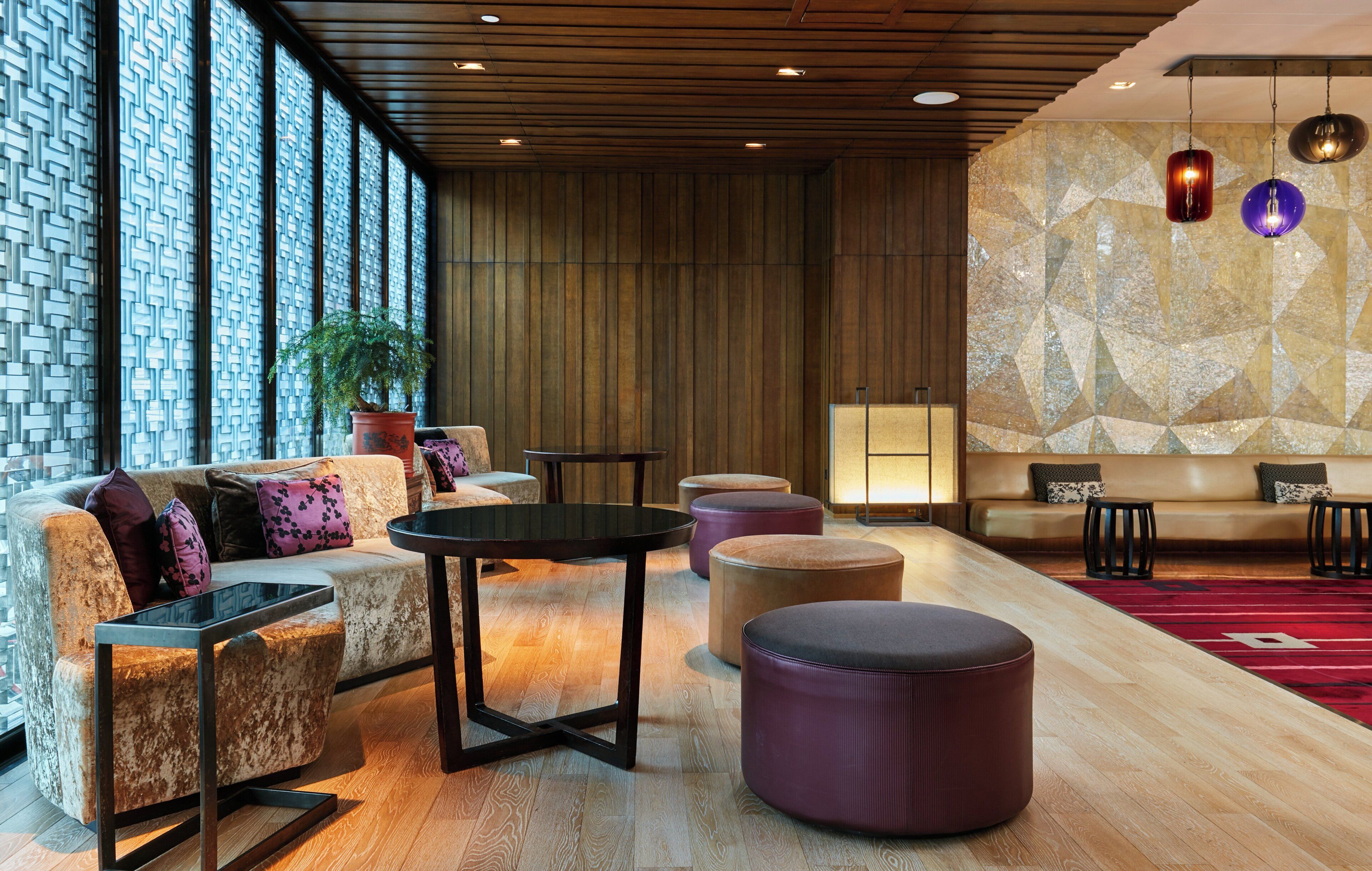A modern lounge area with a sofa, ottomans, a coffee table, and a seating area with a patterned wall and pendant lighting.