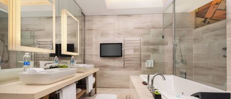A modern bathroom with a large mirror, two sinks, a bathtub, and a TV mounted on the wall.