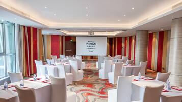 A conference room with white tables and chairs, a large screen displaying 'HOTEL INDIGO', and a patterned carpet.