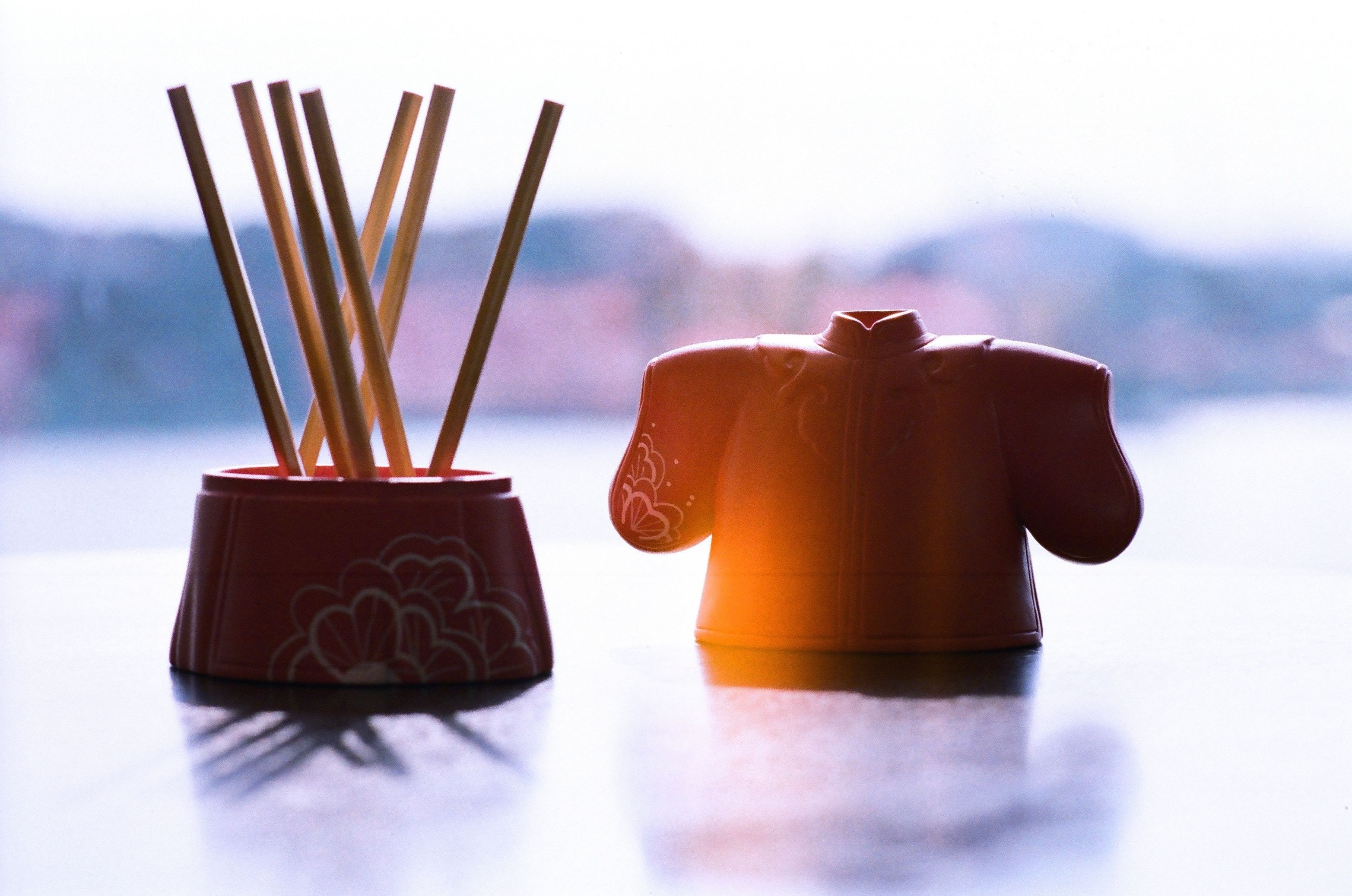Two ceramic containers with wooden sticks, one with a floral design and the other with a figure design, placed on a reflective surface.