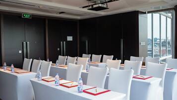 Un salón de conferencias con mesas y sillas blancas, equipado con botellas de agua y tarjetas de identificación.