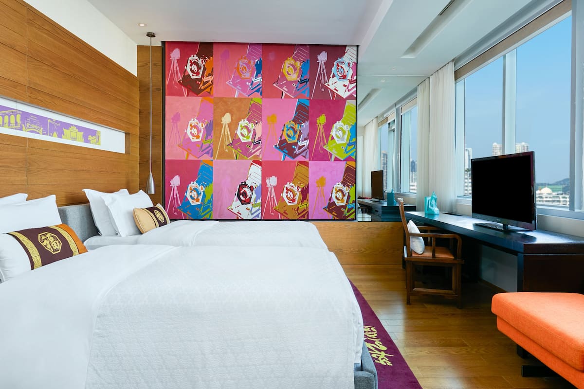 Una habitación de hotel moderna con una cama grande, un escritorio, un televisor y vistas a la ciudad.