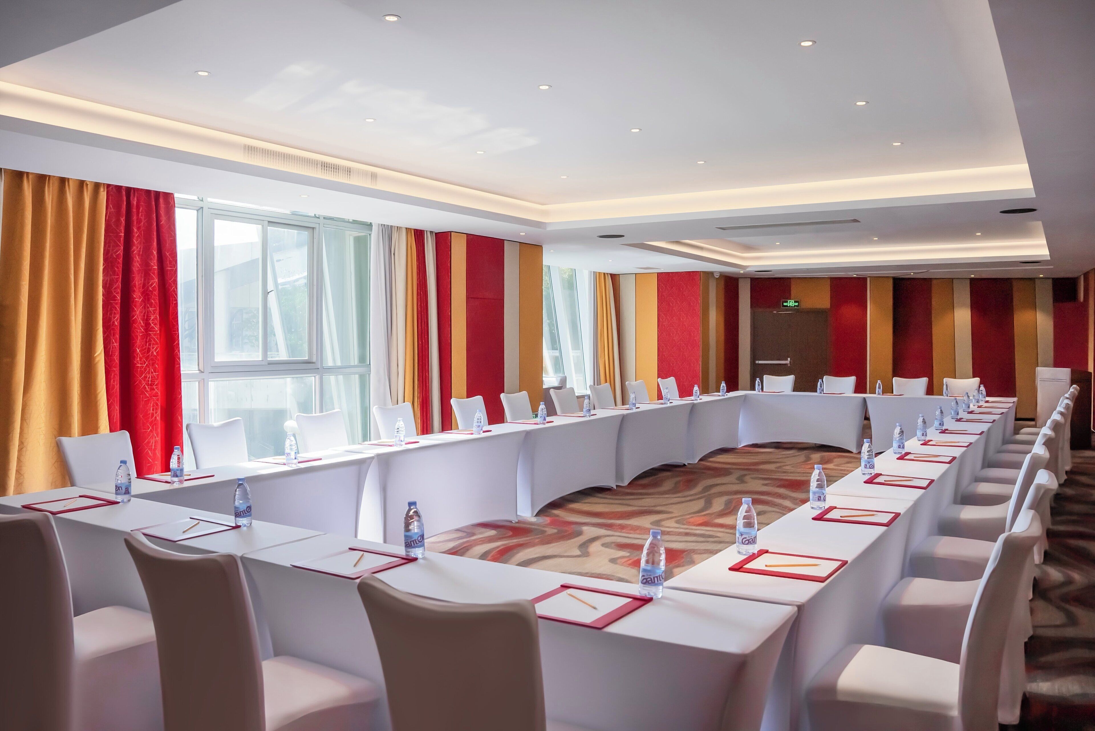 A conference room with a long table, white chairs, and red and yellow curtains.