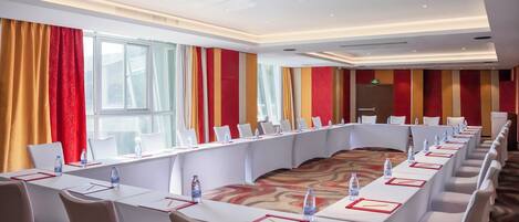 A conference room with a long table, white chairs, and red and yellow curtains.