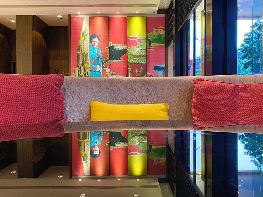 A lobby with a reflective floor, a central seating area with a yellow cushion, and colorful vertical panels in the background.