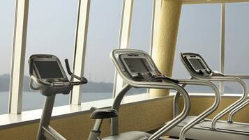 An indoor gym with exercise equipment and large windows overlooking a body of water.