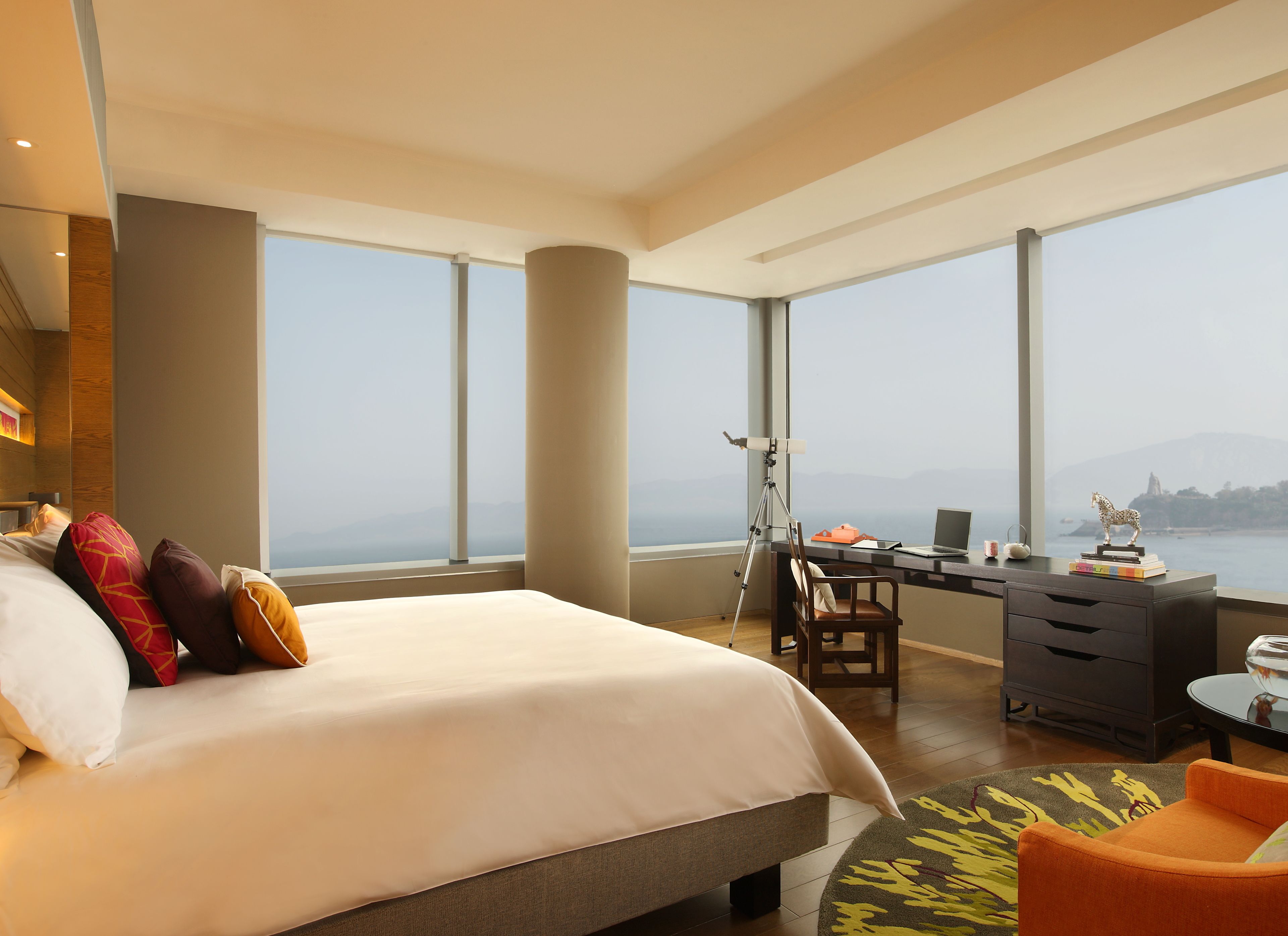 Una habitación de hotel moderna con una cama grande, un escritorio con una computadora portátil y vista al mar.