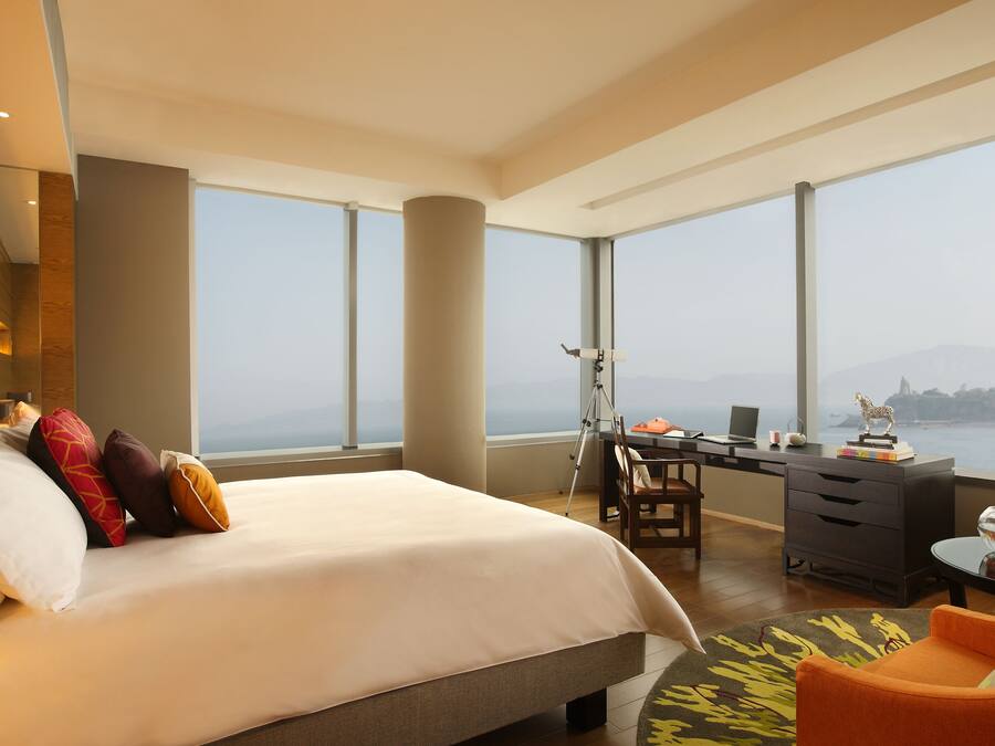 Una habitación de hotel moderna con una cama grande, un escritorio con una computadora portátil y vista al mar.