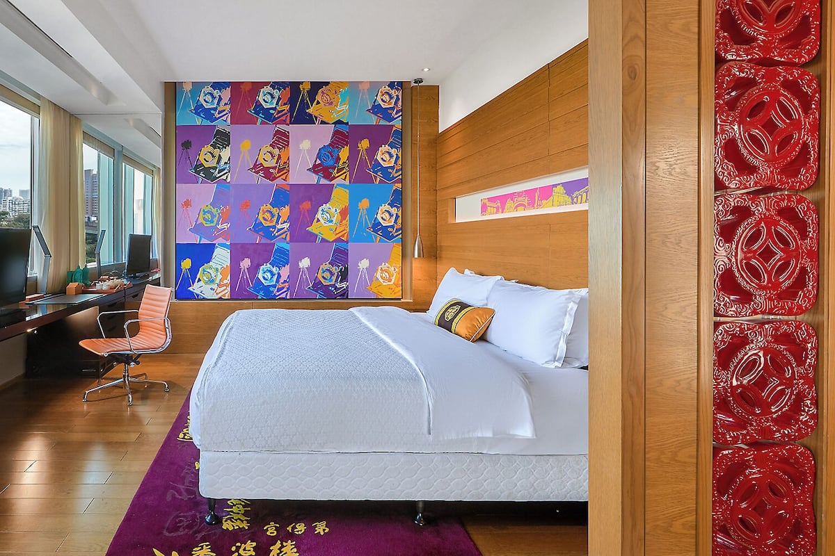 Habitación de hotel moderna con una cama grande, un escritorio con ordenador, televisión y un cuadro abstracto de colores en la pared.