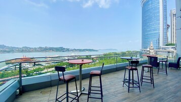Terraço no terraço com vista para um porto, com uma mesa e cadeiras, e um edifício alto ao fundo.