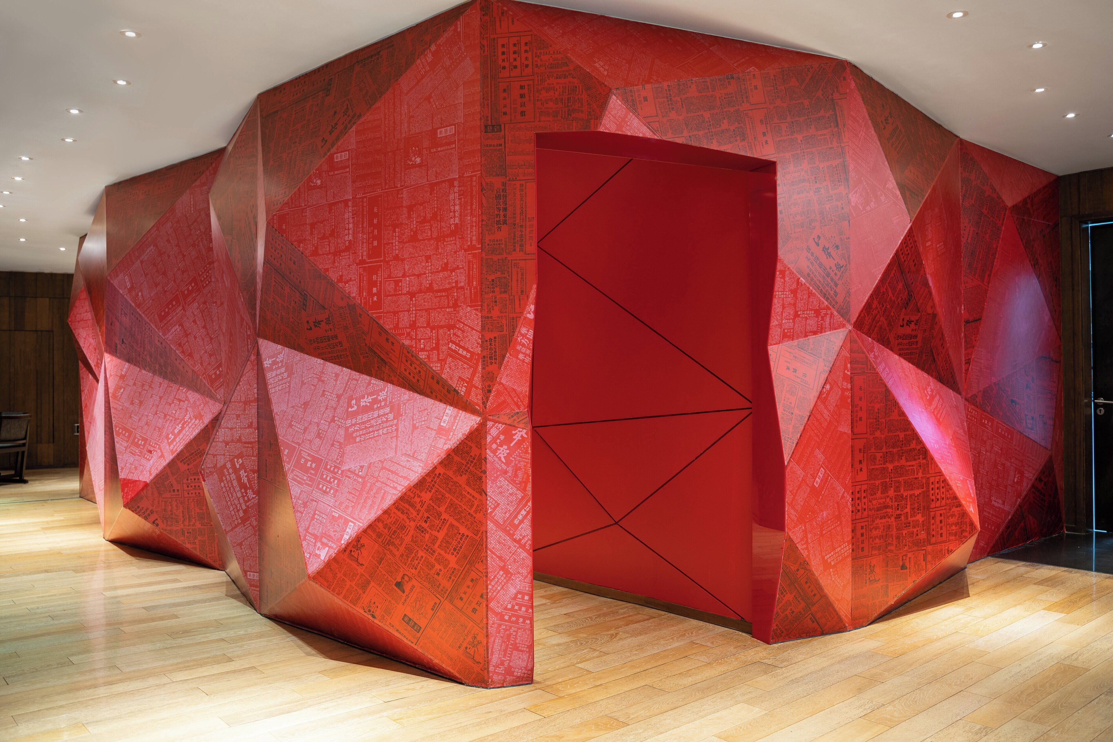 A modern interior with a geometric red wall design and a wooden floor.