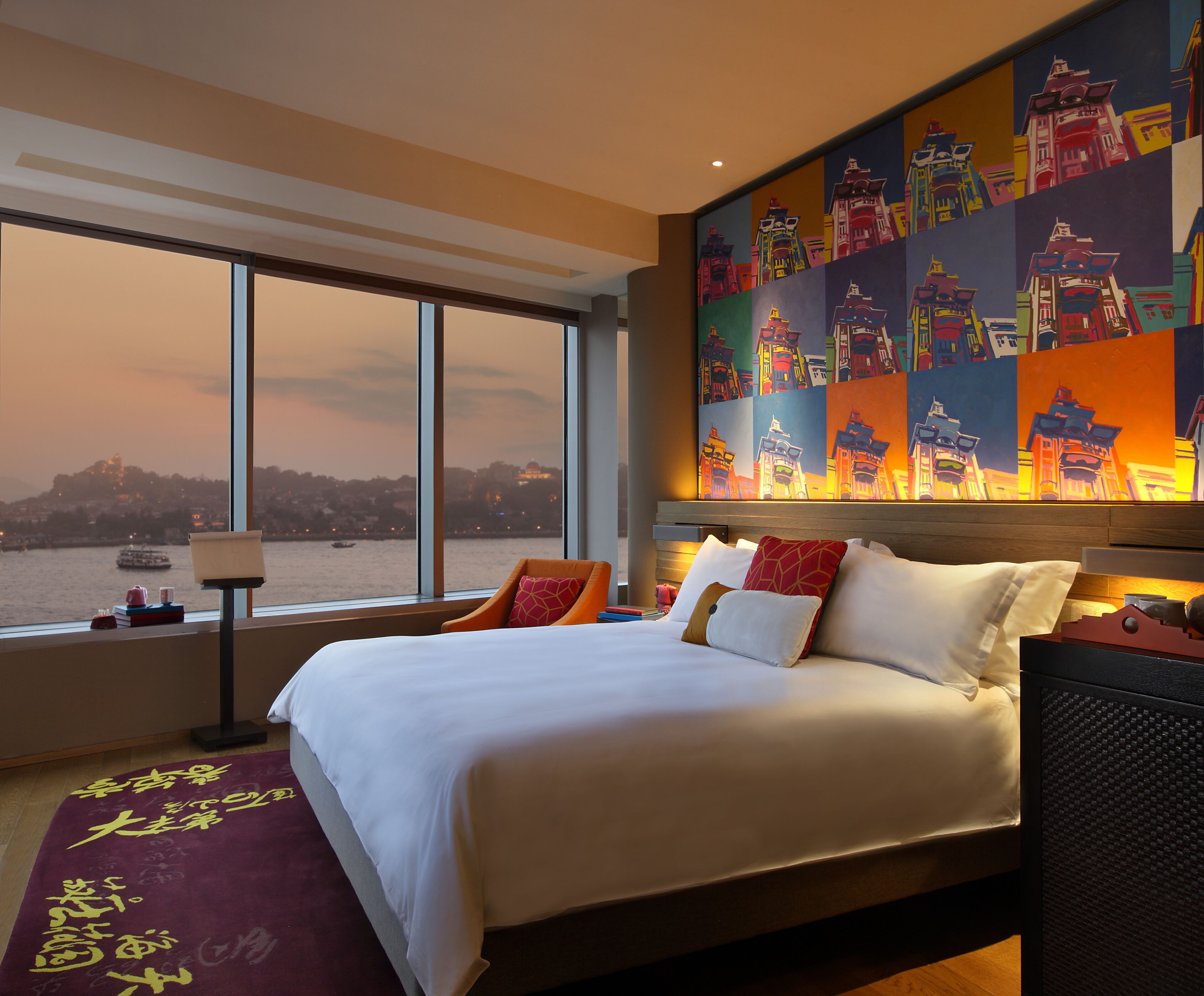 Una habitación de hotel con una cama grande, vista al río y un mural colorido en la pared.