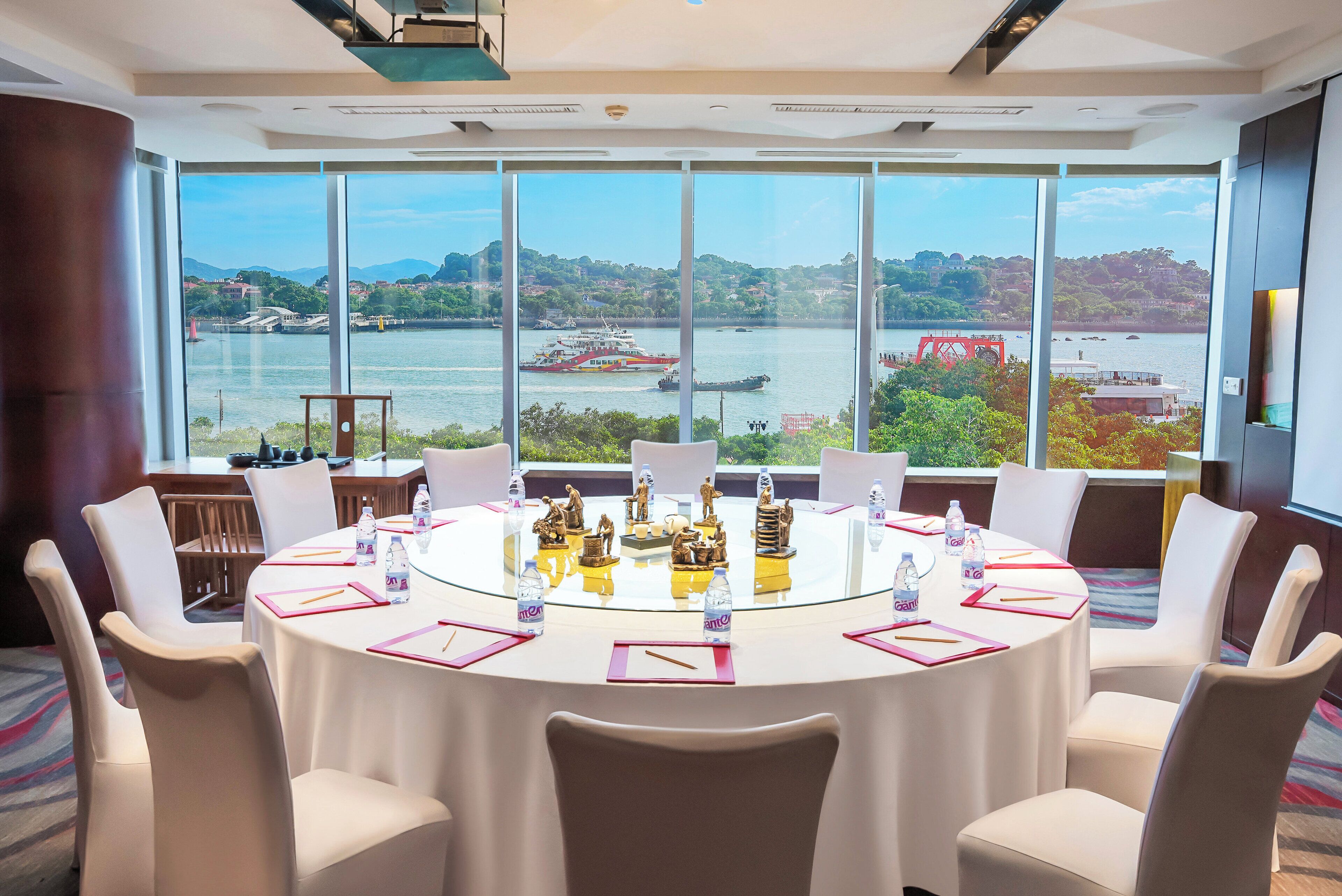 Un salón de conferencias con una gran mesa, sillas y vistas a un río y colinas.