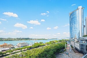 A high-rise hotel with a glass facade, a waterfront view, and a landscaped area with trees.
