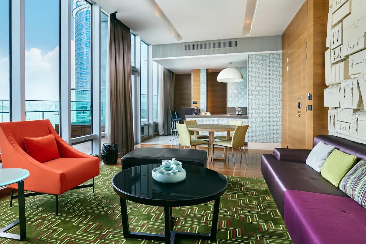 Habitació d'hotel moderna amb una finestra gran, una zona de menjador i una zona d'estar amb un sofà i una butaca.